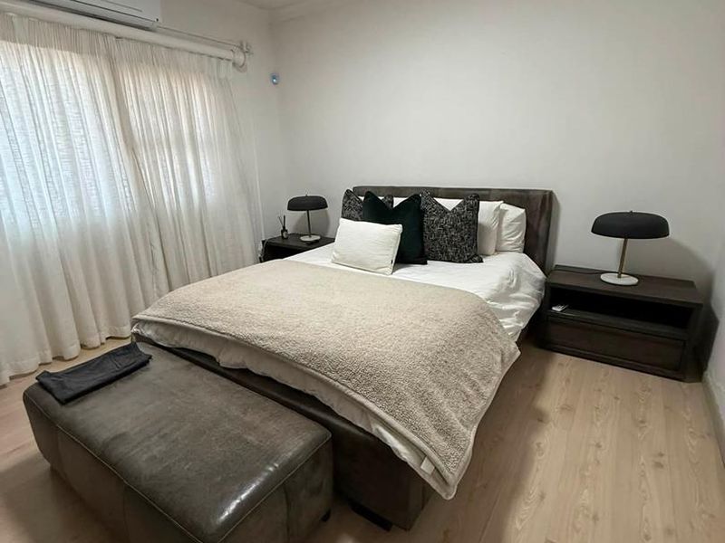 A well-maintained bedroom featuring light-toned laminate flooring and a wall-mounted split-system air conditioning unit.