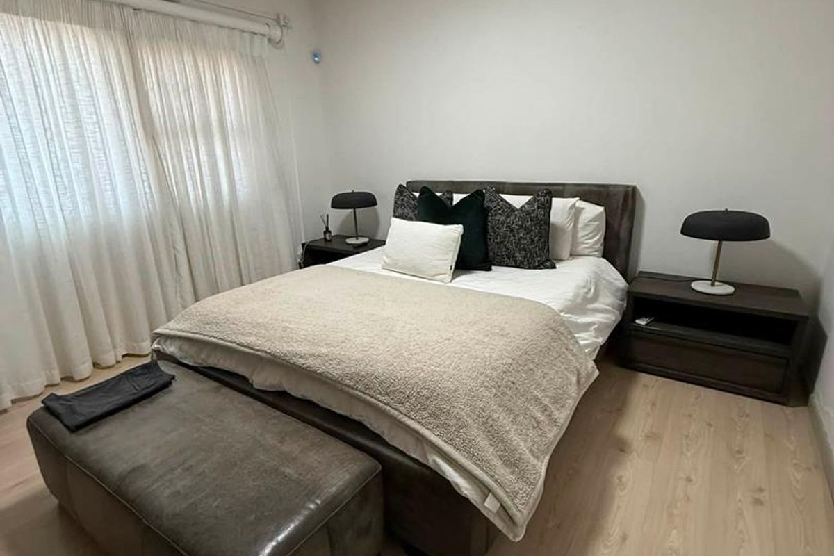 A well-maintained bedroom featuring light-toned laminate flooring and a wall-mounted split-system air conditioning unit.
