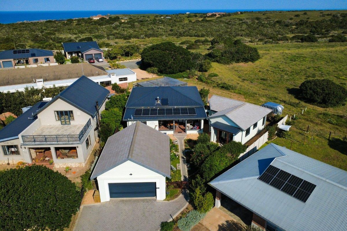 Aerial view of the property showcasing the main residence, detached garage, solar panel installation, and surrounding coastal landscape.