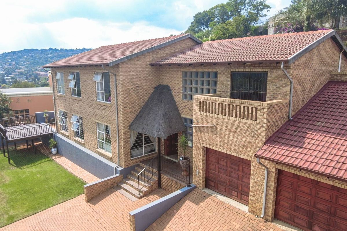 Aerial view of a multi-story face-brick house featuring a tiled roof, double garage, balcony, and a landscaped garden with a raised wooden deck.