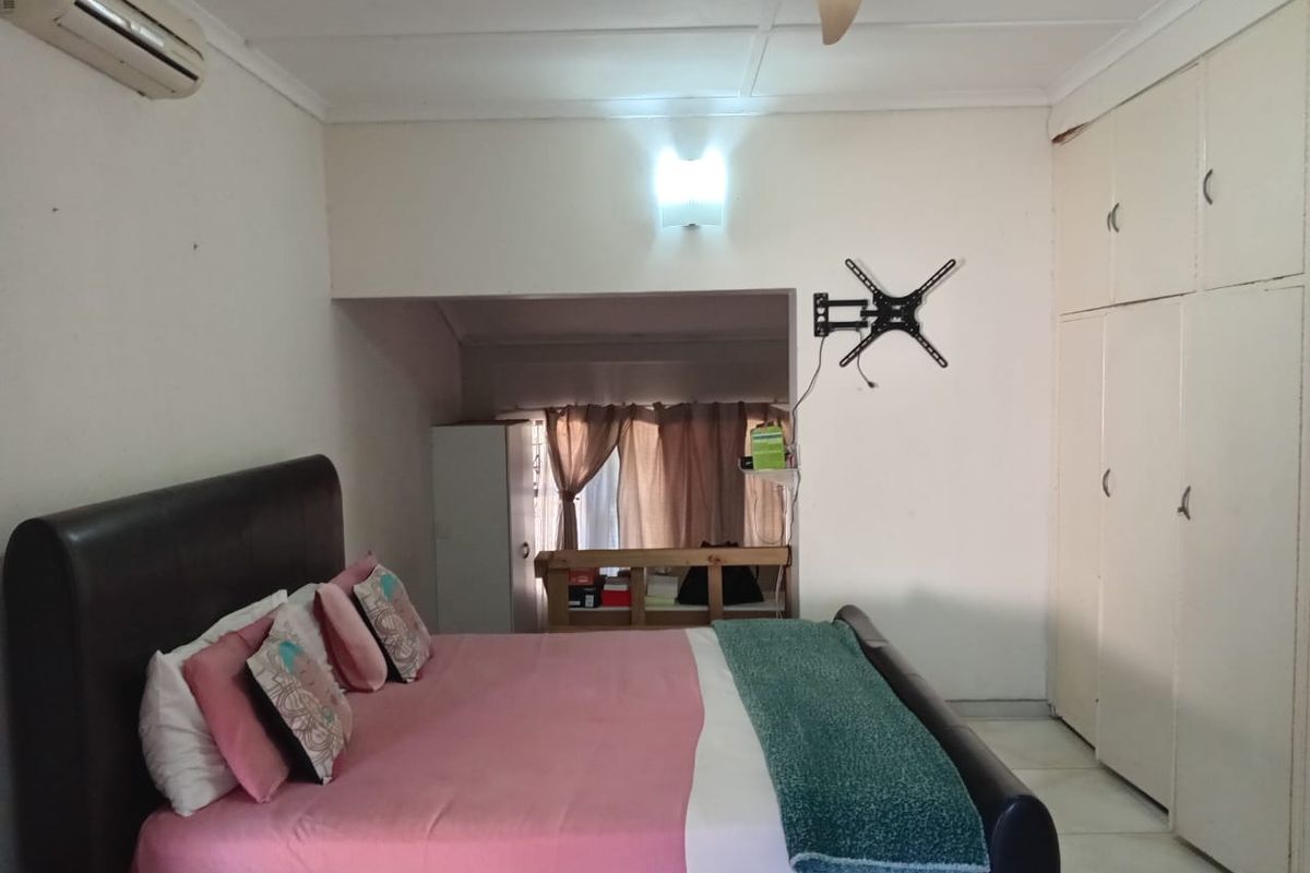 A bedroom featuring built-in floor-to-ceiling cupboards, a ceiling fan, and a wall-mounted air conditioning unit.