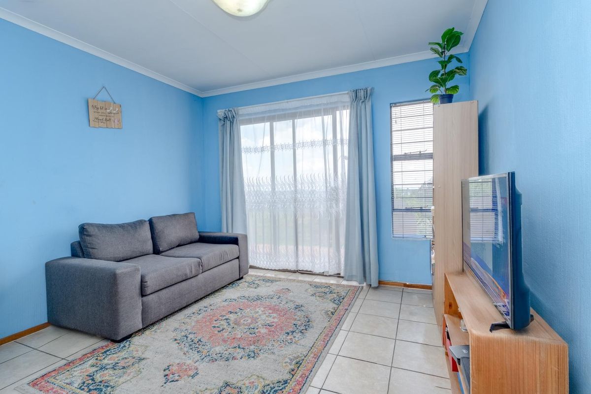 A living room featuring tiled flooring, a sliding glass door providing natural light, and an aluminium window frame.