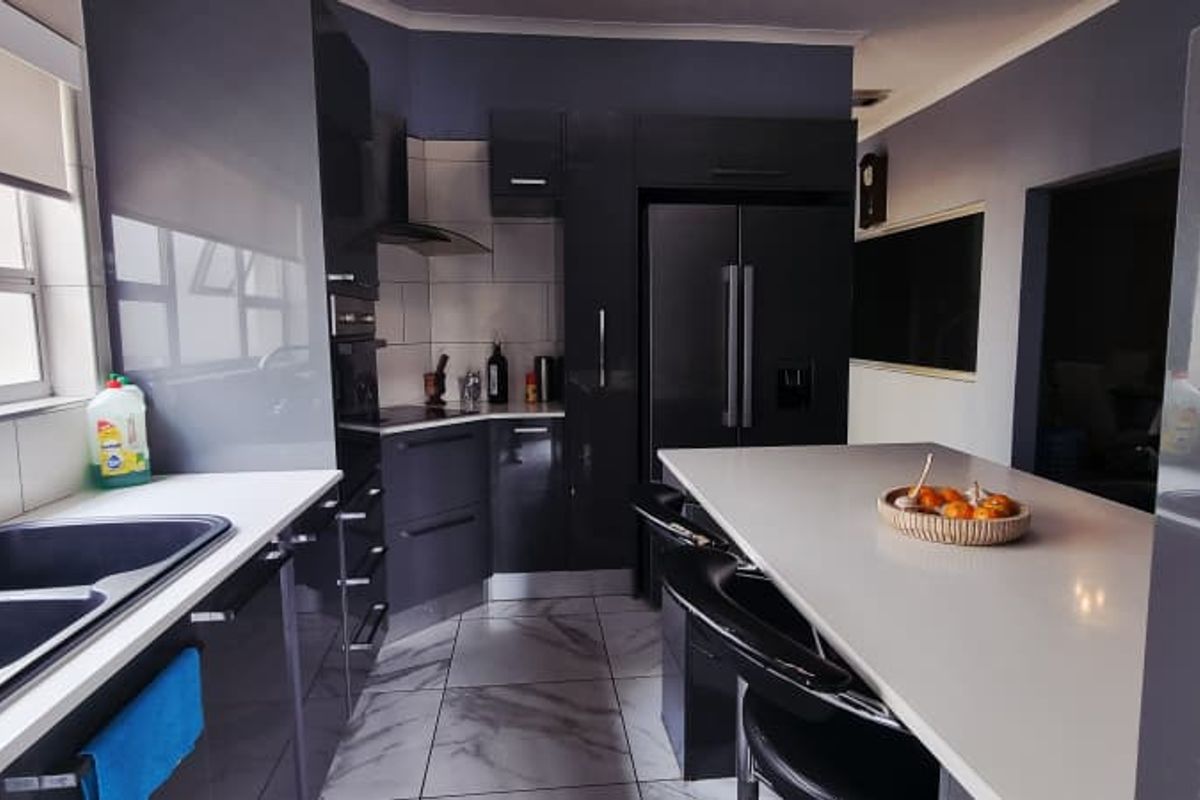 Modern kitchen featuring high-gloss dark cabinetry, stone countertops, a central island with breakfast bar, and marble-look floor tiles.