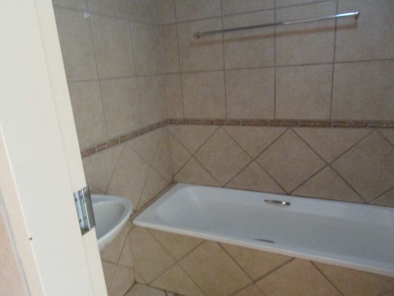 A functional bathroom featuring a built-in bathtub, corner basin, and neutral wall tiling with a decorative border.