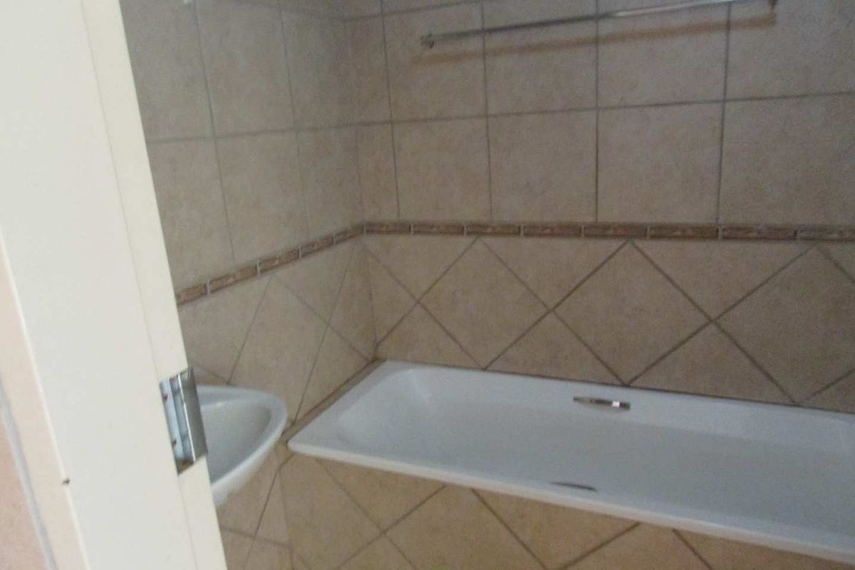 A functional bathroom featuring a built-in bathtub, corner basin, and neutral wall tiling with a decorative border.
