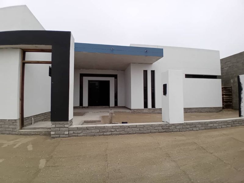 Modern single-story house facade featuring stone cladding and a covered entrance, currently undergoing final exterior construction and landscaping.