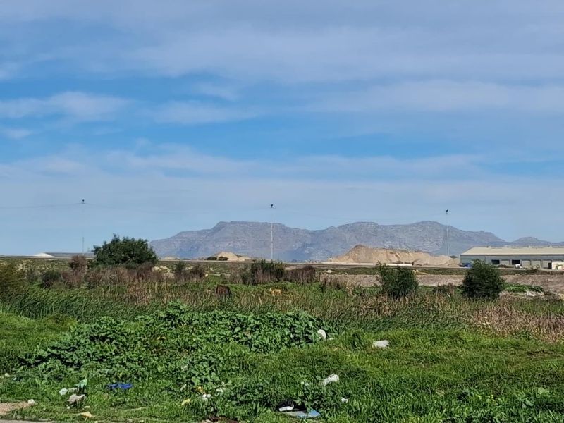 A scenic view of open agricultural land with distant mountain ranges and surrounding industrial infrastructure.