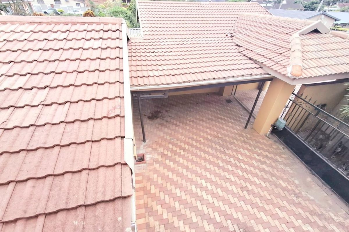 An elevated aerial view of the property showing the tiled roof, paved driveway, and covered carport area.