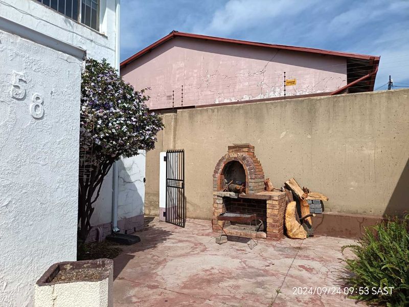 Rear courtyard area featuring a brick built-in braai, perimeter wall with electric fencing, and paved flooring, offering a private outdoor space.