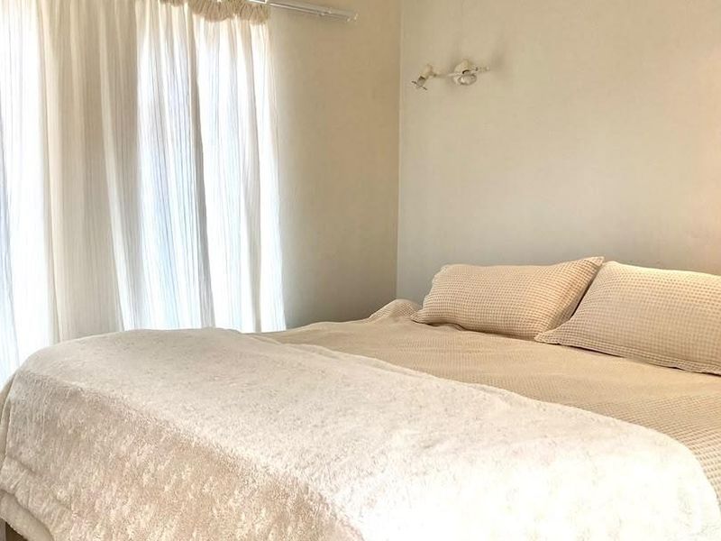 A neutrally decorated bedroom featuring a wall-mounted light fixture and window treatments.