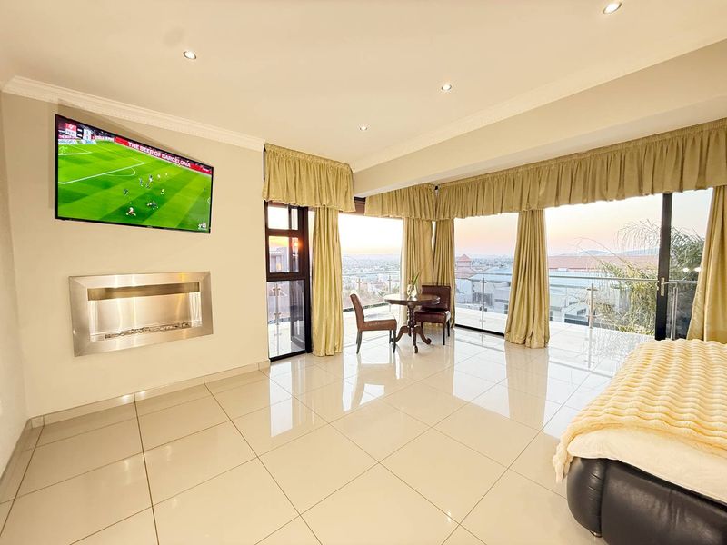 Spacious bedroom featuring polished tile floors, a modern wall-mounted fireplace, and large sliding glass doors opening to a balcony with expansive views.