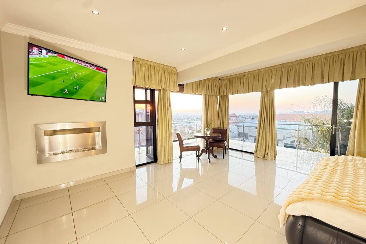 Spacious bedroom featuring polished tile floors, a modern wall-mounted fireplace, and large sliding glass doors opening to a balcony with expansive views.