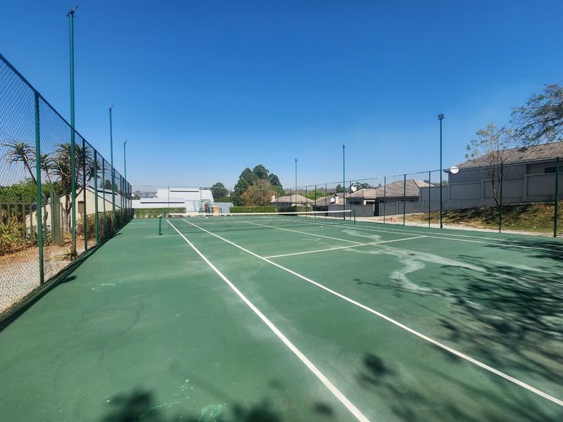 A well-maintained outdoor tennis court featuring chain-link perimeter fencing, integrated floodlights, and a standard tennis net.