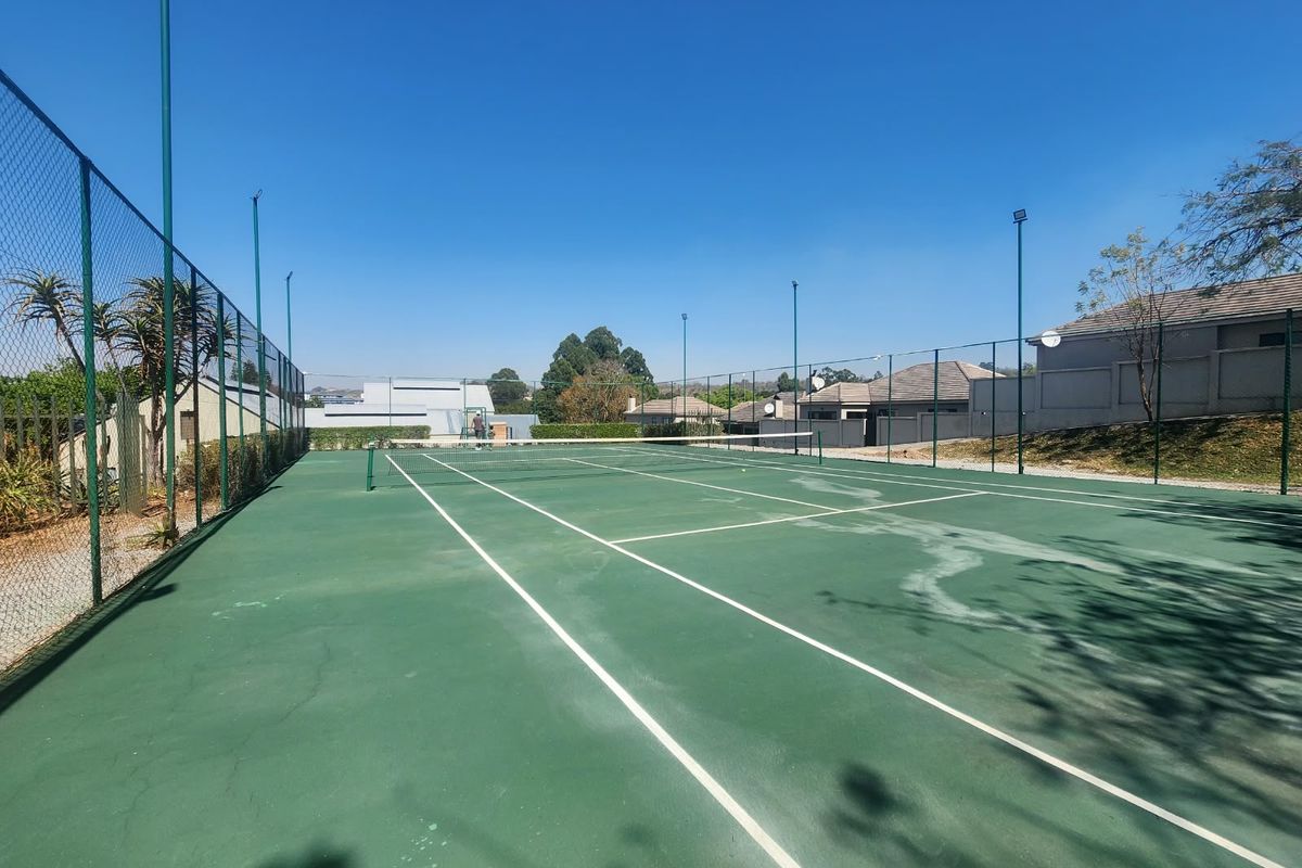 A well-maintained outdoor tennis court featuring chain-link perimeter fencing, integrated floodlights, and a standard tennis net.