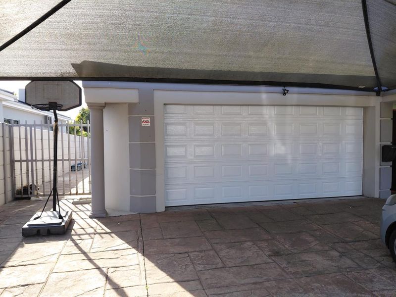 A secure garage featuring a white sectional door, paved driveway, and a protective shade cloth canopy, providing convenient covered parking.