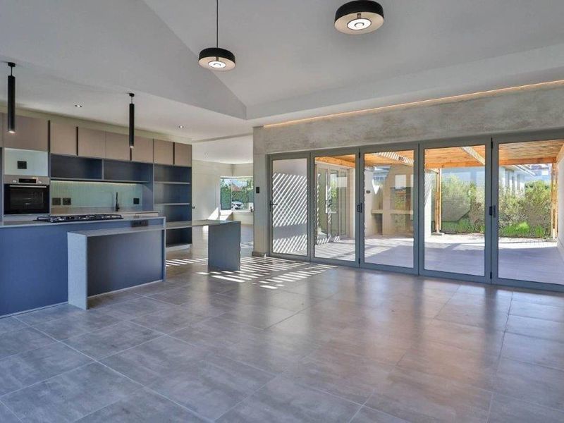 Modern open-plan kitchen and living area featuring sleek cabinetry, built-in appliances, large format floor tiles, and seamless access to the outdoor patio through stacking doors.