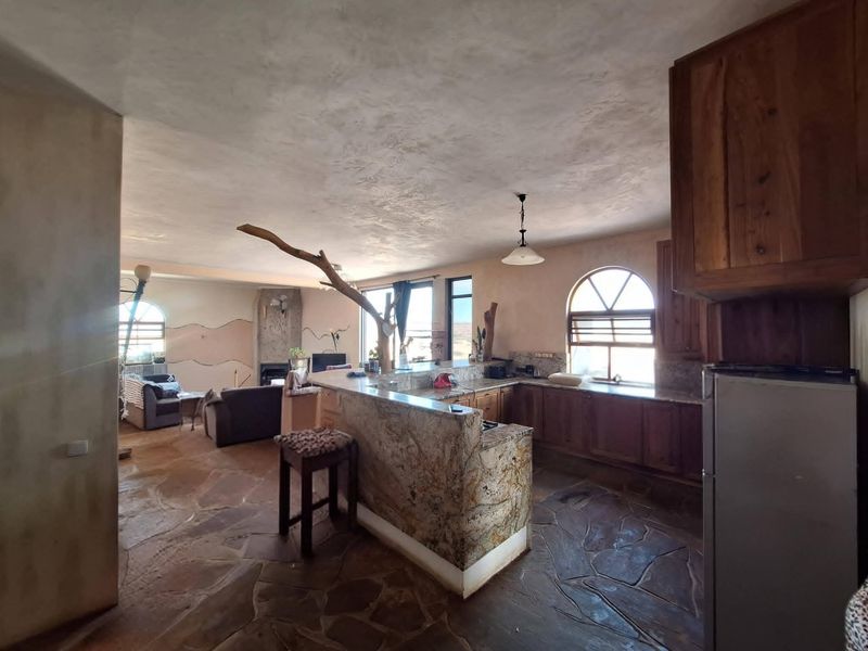 Spacious open-plan living and kitchen area featuring rustic stone flooring, granite countertops, wooden cabinetry, and unique arched windows with a built-in fireplace.
