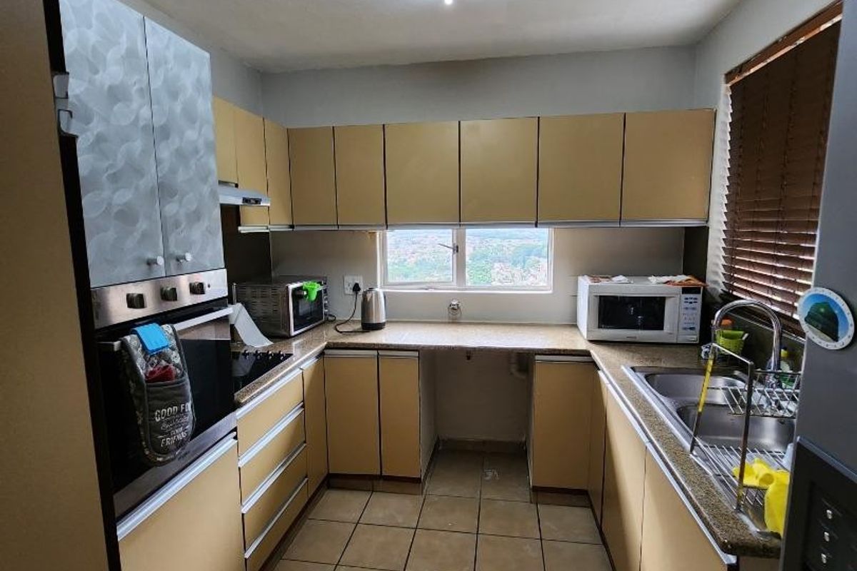 A functional U-shaped kitchen featuring built-in cabinetry, laminate countertops, a double basin sink, and integrated cooking appliances with tiled flooring.