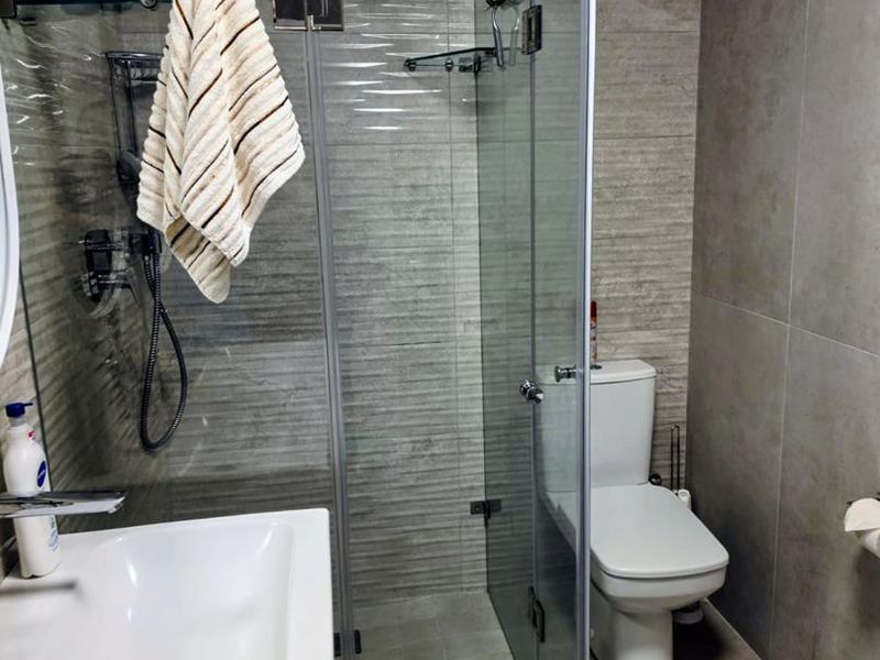 Modern bathroom featuring a glass-enclosed shower with rain shower head, wall-mounted basin, and ceramic toilet with neutral tiled finishes.