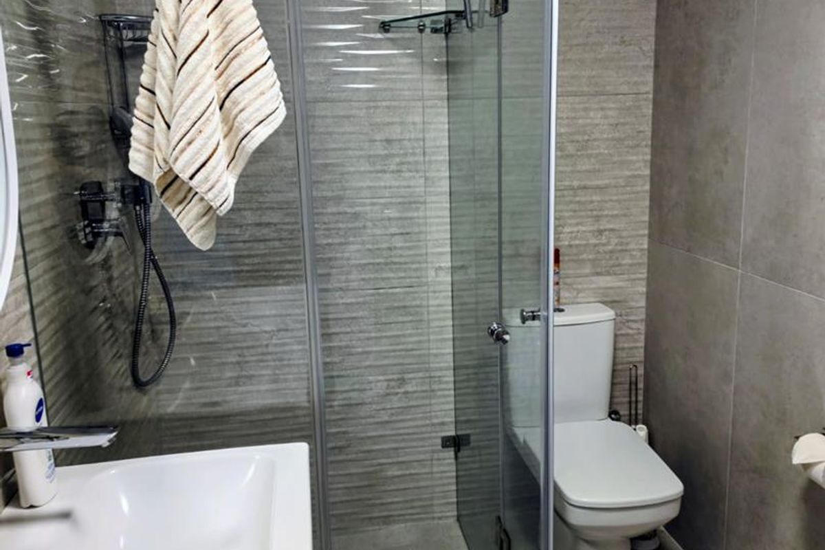 Modern bathroom featuring a glass-enclosed shower with rain shower head, wall-mounted basin, and ceramic toilet with neutral tiled finishes.