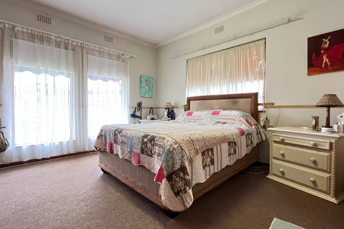 A spacious bedroom featuring neutral walls, carpet flooring, and large windows with curtain tracks, offering a functional and well-lit living space.