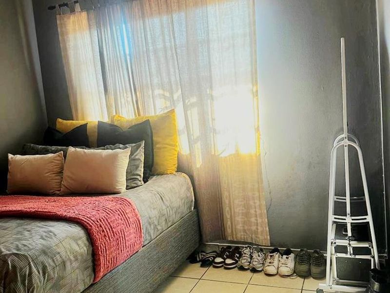 A bedroom featuring tiled flooring and a wall-mounted ventilation grille, with natural light filtering through the window.