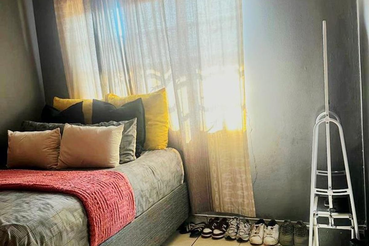 A bedroom featuring tiled flooring and a wall-mounted ventilation grille, with natural light filtering through the window.