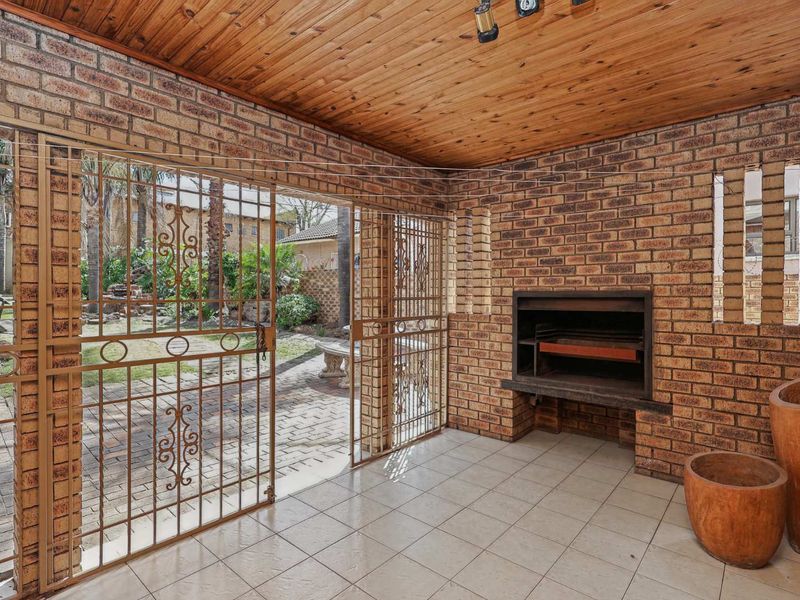 Covered patio area featuring exposed brick walls, a built-in braai, timber ceiling, and tiled flooring, with direct access to the garden.