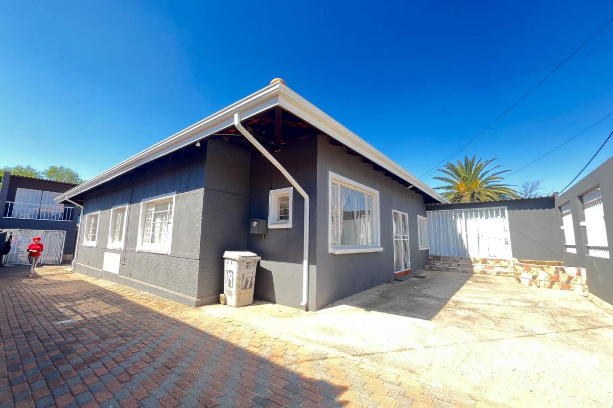 Rear exterior view of the house featuring brick paving, a concrete patio area, and secure gated access.