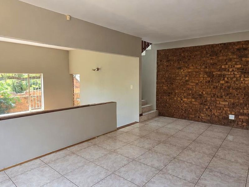 Spacious living area featuring an exposed brick accent wall, neutral ceramic floor tiles, and a staircase leading to the upper level.