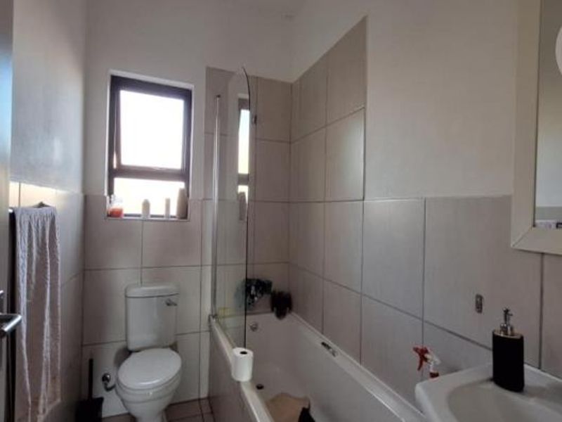 A functional bathroom featuring a bathtub with a glass screen, pedestal basin, toilet, and neutral wall tiling.