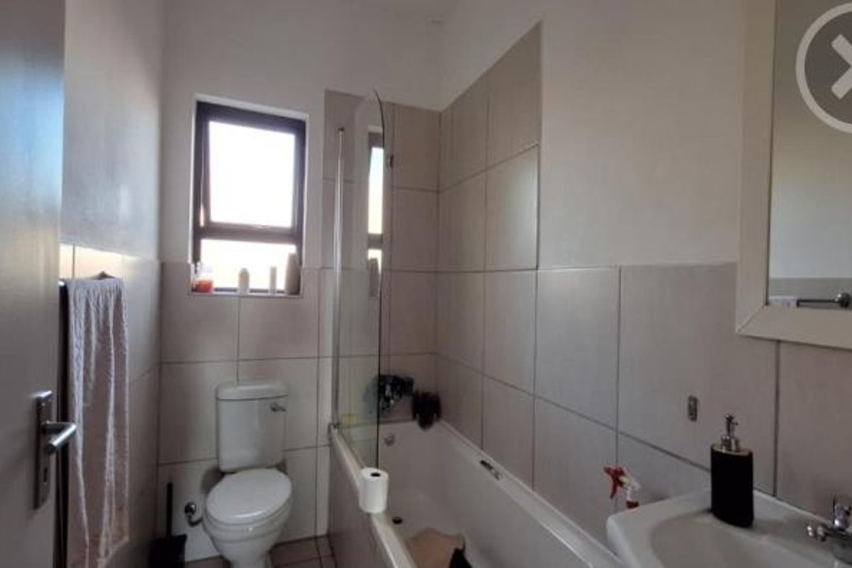 A functional bathroom featuring a bathtub with a glass screen, pedestal basin, toilet, and neutral wall tiling.