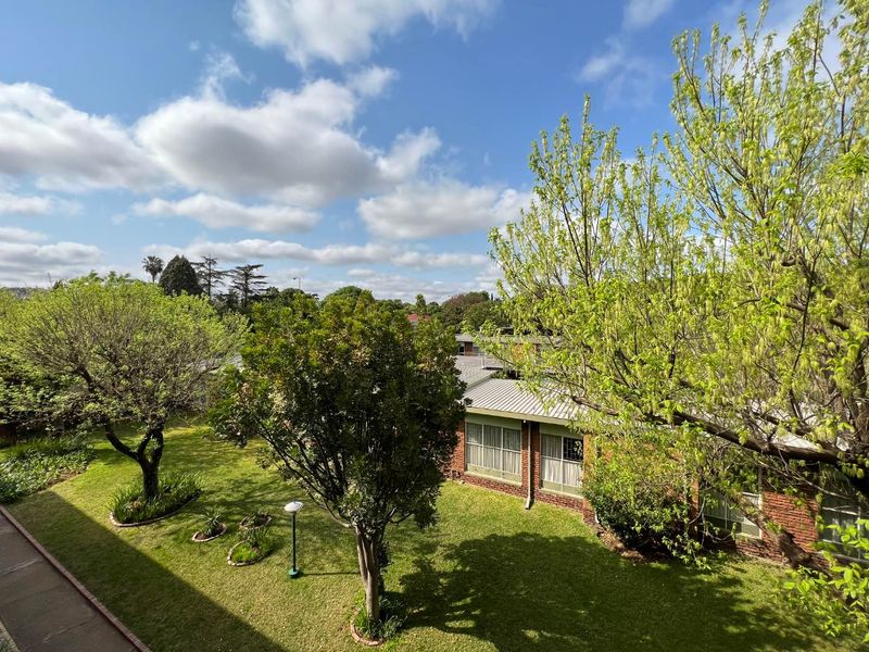 An elevated view overlooking a well-maintained communal garden area with mature trees and the brick facade of an adjacent apartment building.
