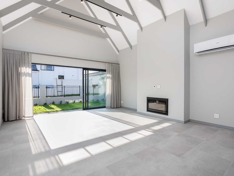 Spacious living room featuring a high vaulted ceiling with exposed rafters, a modern built-in fireplace, and large sliding glass doors opening to the garden.