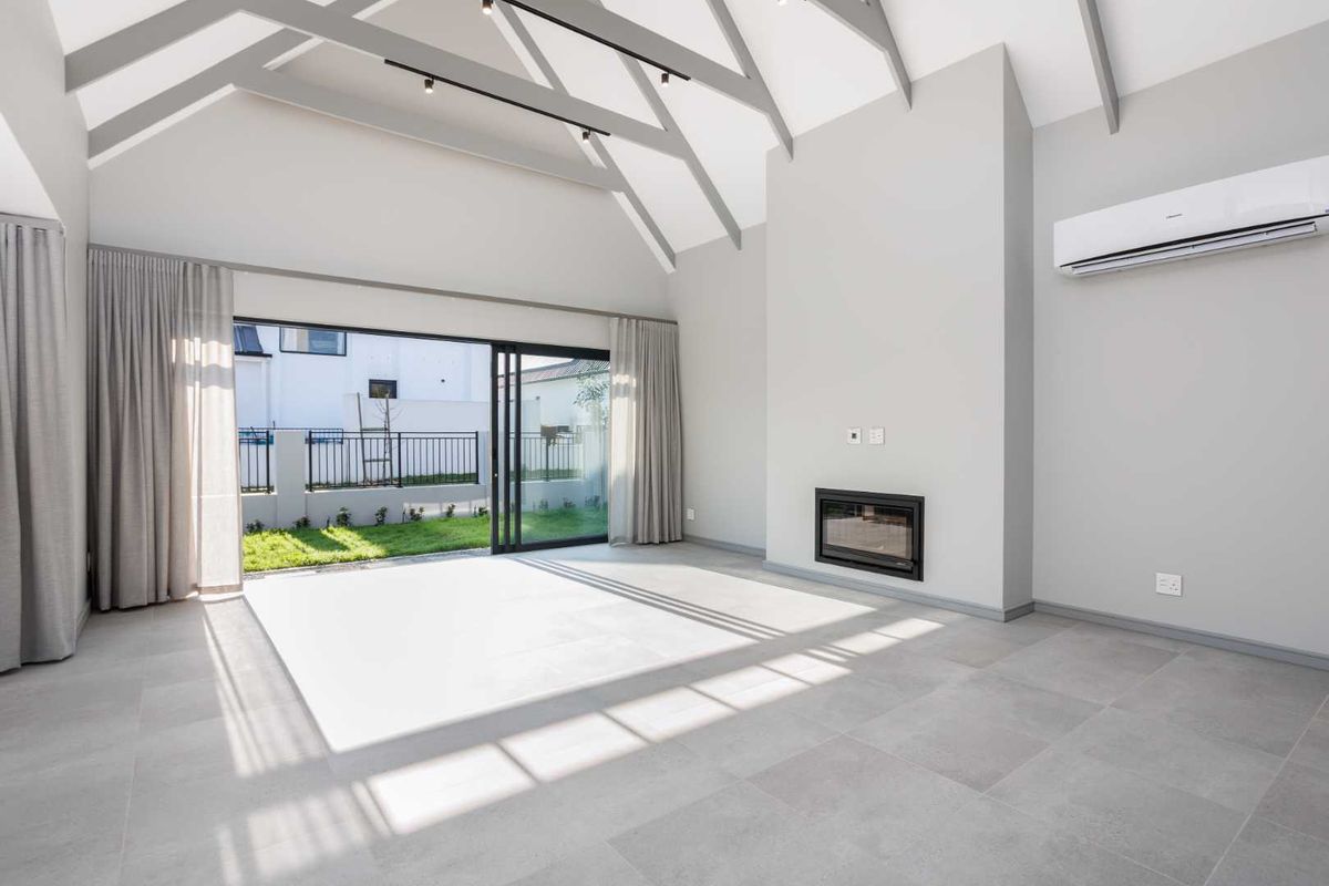 Spacious living room featuring a high vaulted ceiling with exposed rafters, a modern built-in fireplace, and large sliding glass doors opening to the garden.