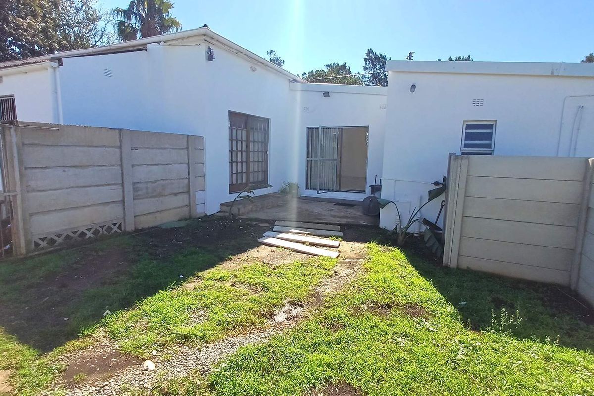 Rear exterior view of the property featuring a small garden area, concrete boundary walls, and access to the home via sliding glass doors.