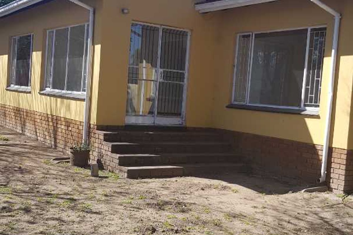 Rear exterior view of the house featuring a brick base, concrete steps, and security gate access, set against a large unlandscaped yard.