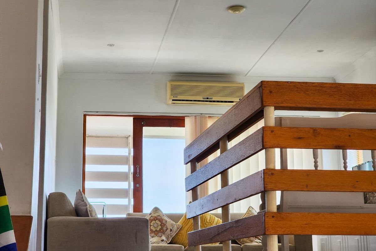 A view of a living area featuring a wooden staircase railing, a wall-mounted air conditioning unit, and a sliding door leading to an outdoor space.