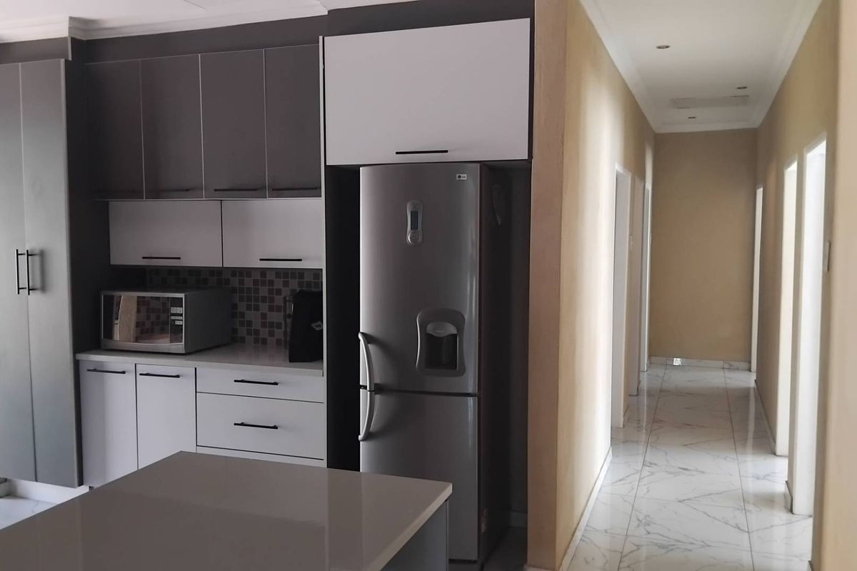 Modern kitchen featuring two-tone cabinetry, stone countertops, and a tiled backsplash, leading into a bright hallway with marble-look floor tiles.