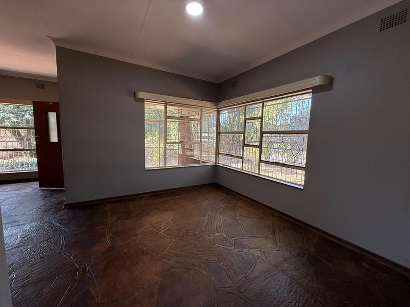 A bright, empty living room featuring unique stone flooring, corner windows with security bars, and neutral grey walls.