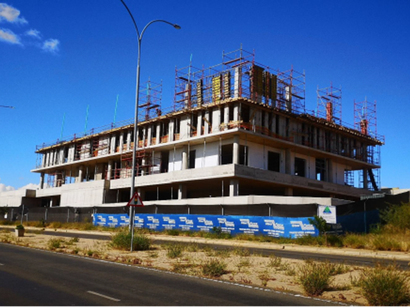 A large commercial building currently under construction, featuring a concrete frame and extensive scaffolding visible from the street.