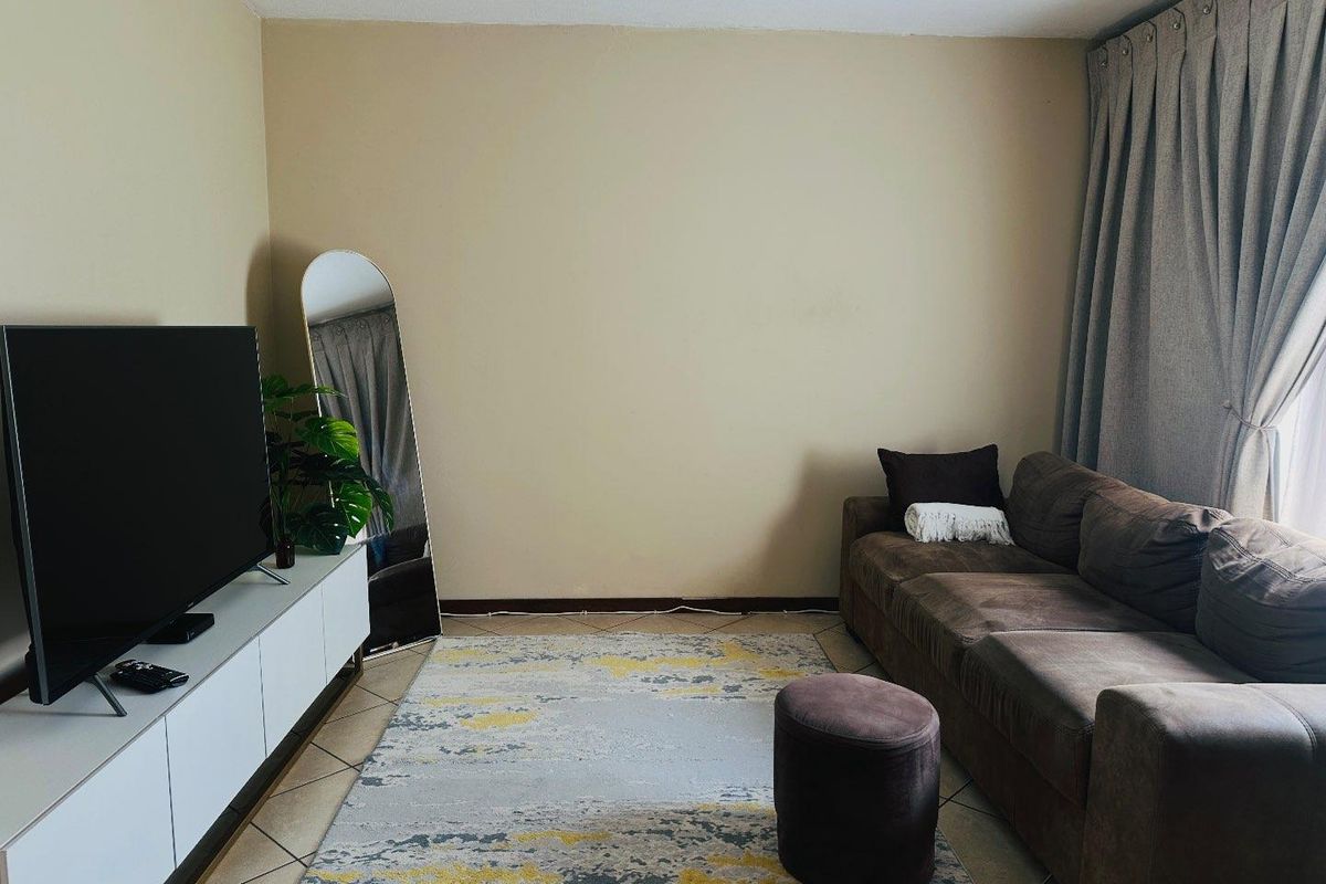 A comfortable living room featuring neutral wall tones, tiled flooring, and large window curtains, providing a functional and inviting space.