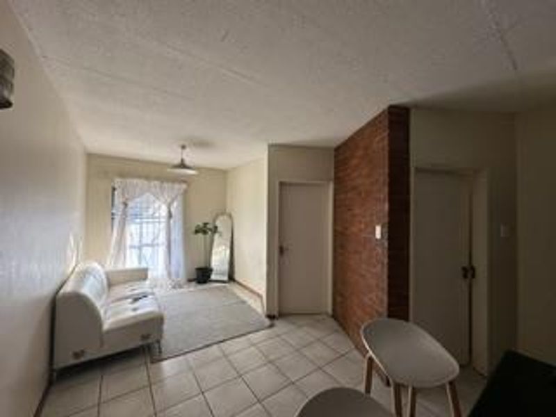 Open plan living area featuring a distinctive exposed brick wall, ceramic tiled flooring, and neutral wall finishes.