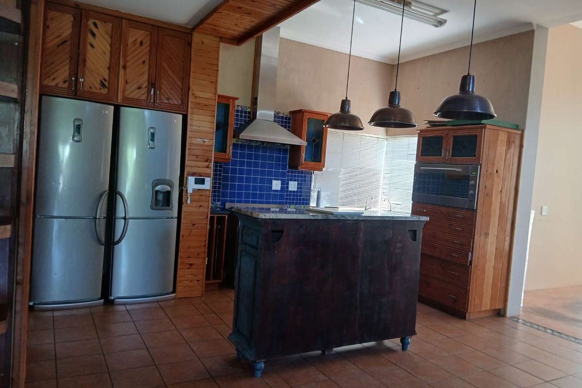 A rustic kitchen featuring wooden cabinetry, a central island, blue tiled backsplash, stainless steel extractor fan, and built-in oven.