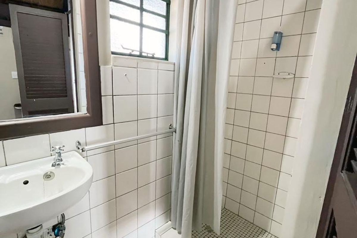A compact hotel bathroom featuring a tiled shower enclosure, pedestal basin, and terracotta floor tiles with a classic rustic aesthetic.