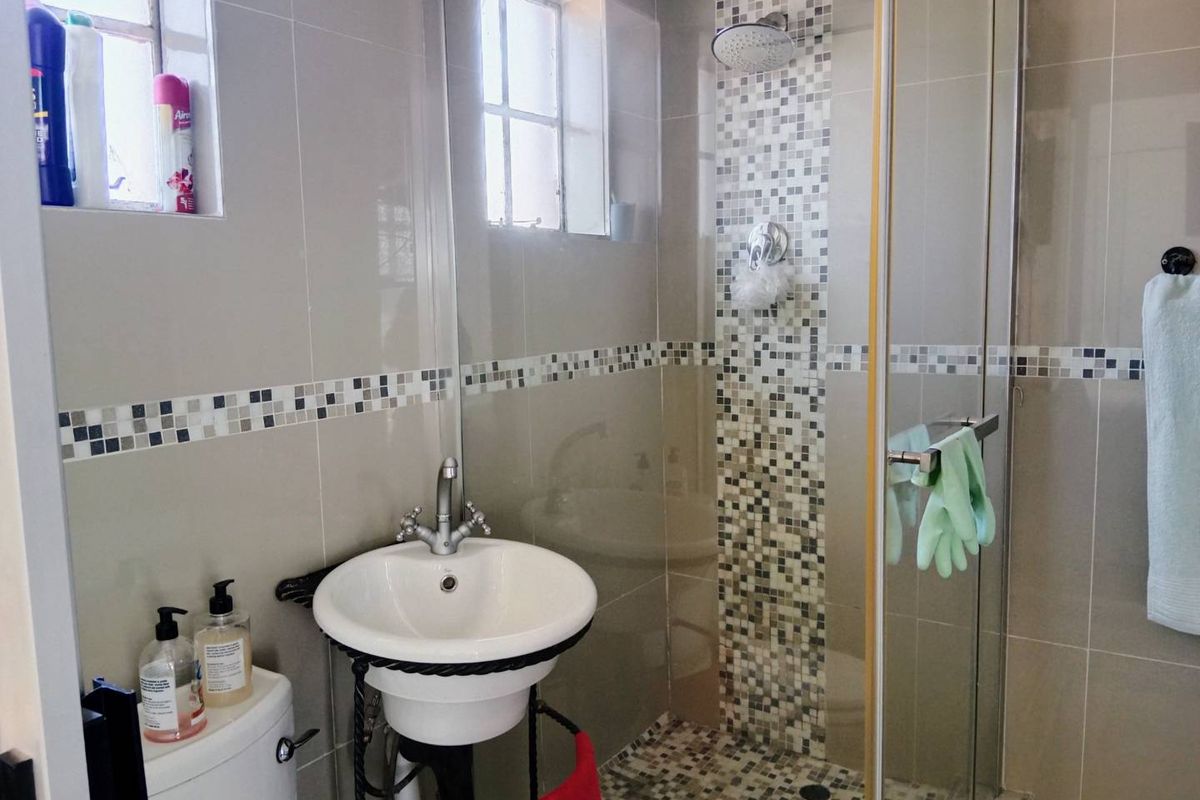 A compact bathroom featuring a pedestal sink, a glass-enclosed shower with mosaic tile accents, and neutral wall tiling.