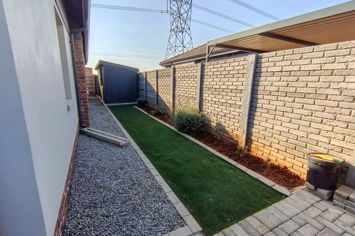 A side garden area featuring a gravel path, artificial lawn, brick boundary wall, and a metal storage shed.
