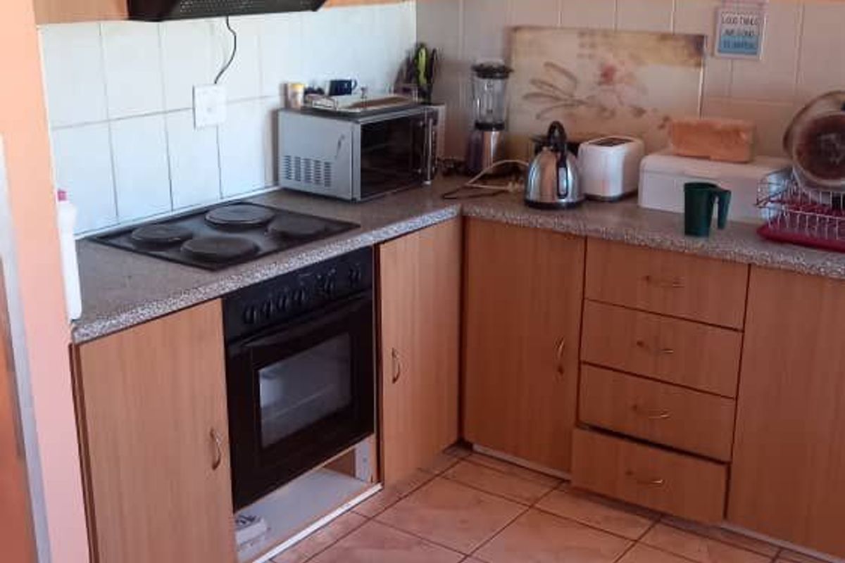 A functional kitchen featuring laminate cabinetry, a built-in oven with electric hob, extractor fan, and tiled flooring.