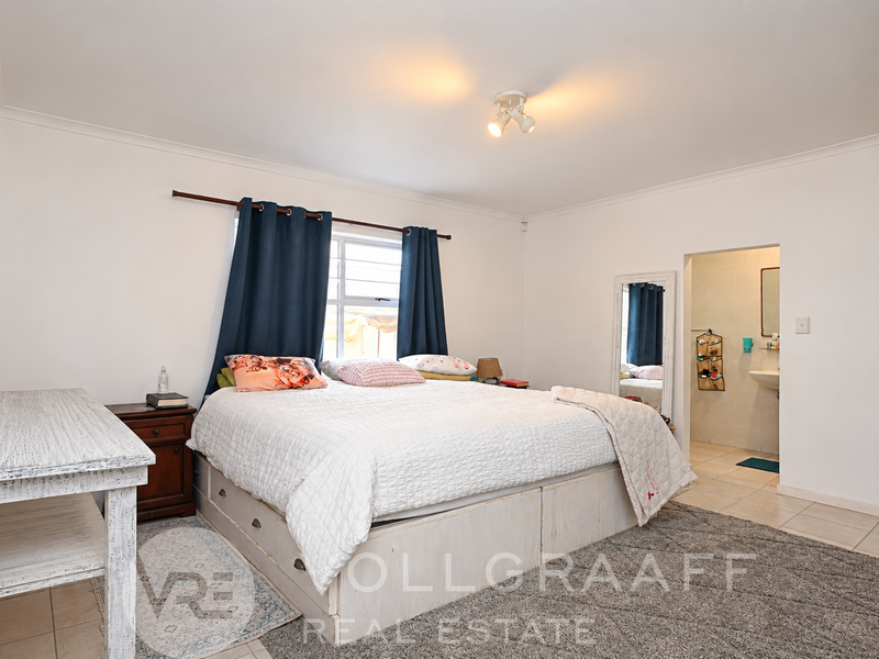 Spacious bedroom featuring neutral walls, tiled flooring, and an attached en-suite bathroom, offering a comfortable and functional living space.