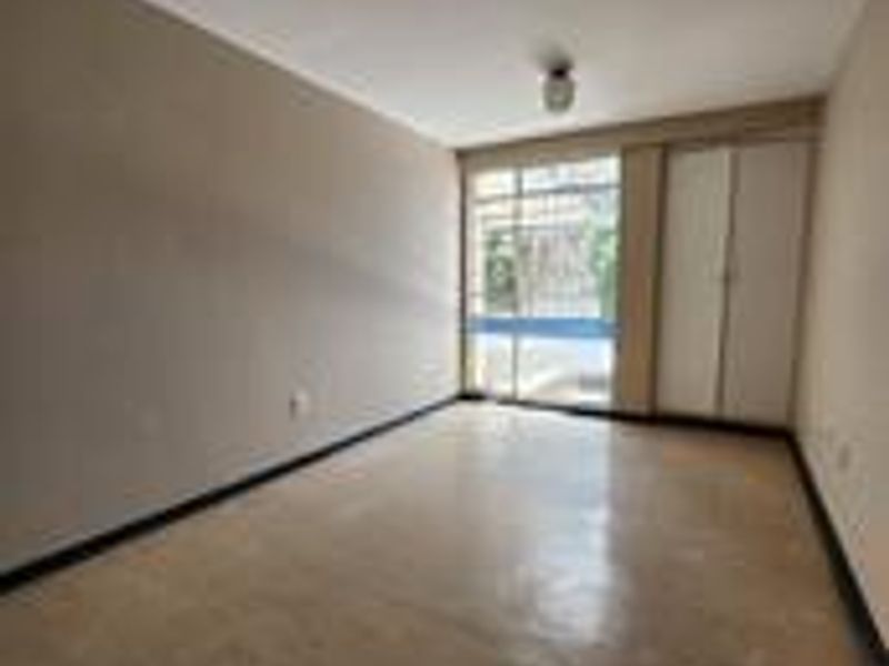 An empty bedroom featuring a built-in wardrobe, large window for natural light, and neutral wall finishes.
